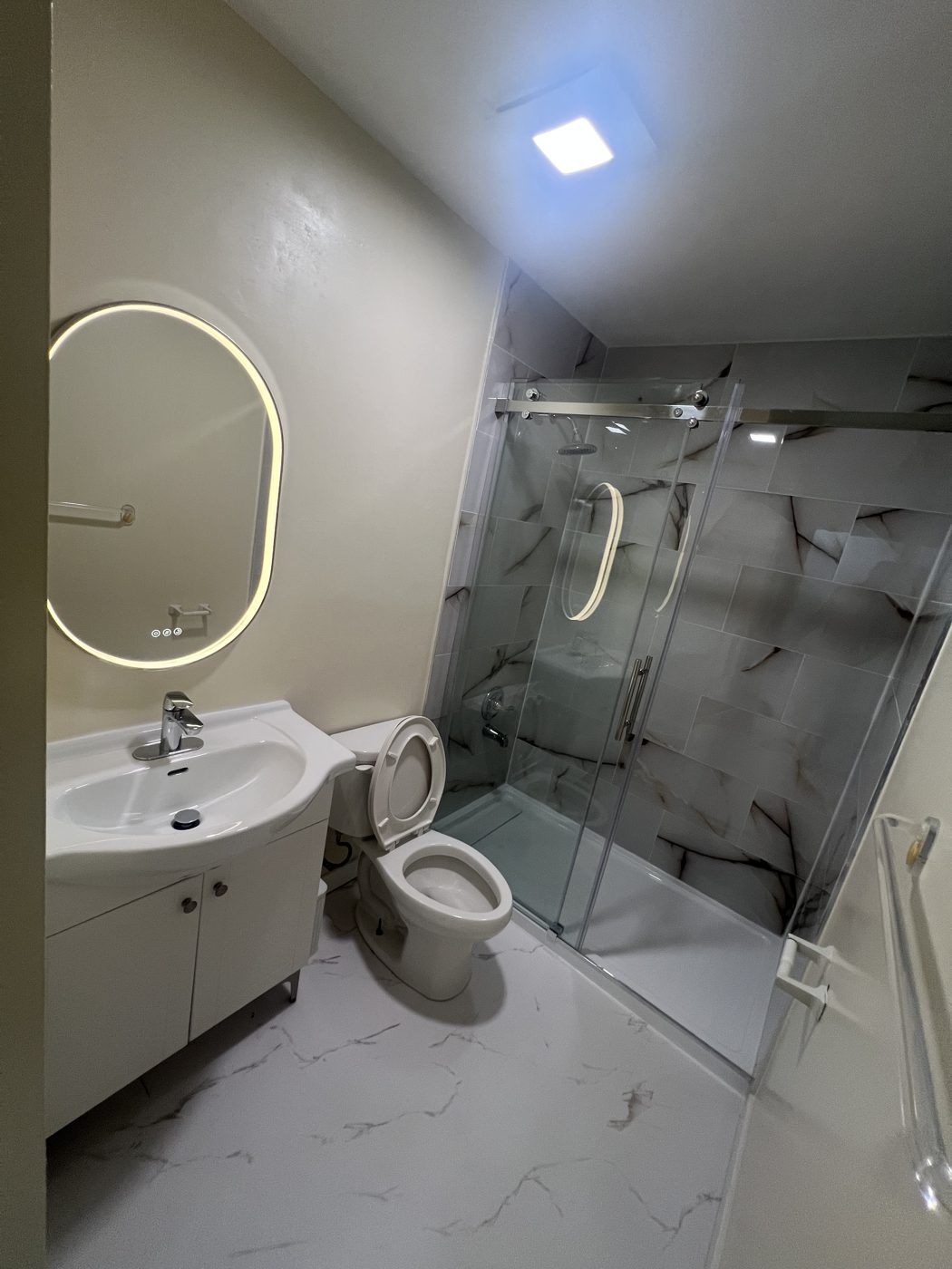 Bathroom after: glass shower, marble-look tile and new vanity